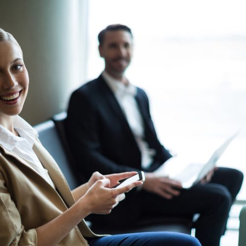 Portrait of smiling commuters sitting in waiting area at airport terminal