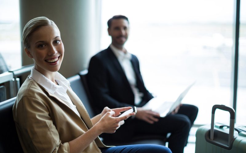 Portrait of smiling commuters sitting in waiting area at airport terminal